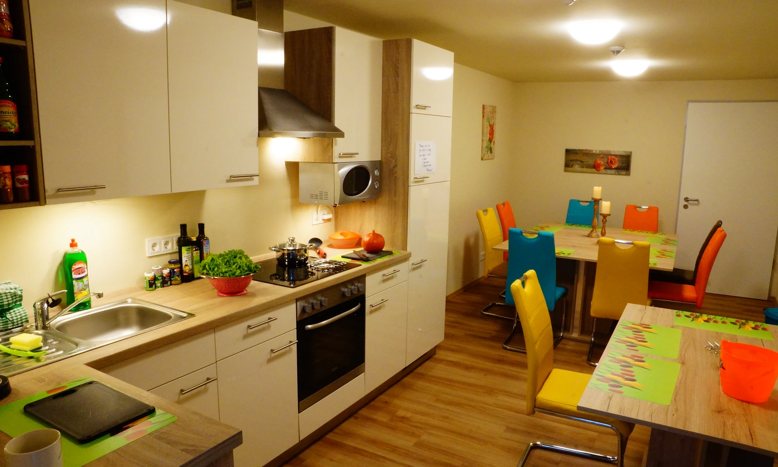 Gemeinschaftsküche mit Herd, Kühlschrank und Esstischen mit bunten Stühlen