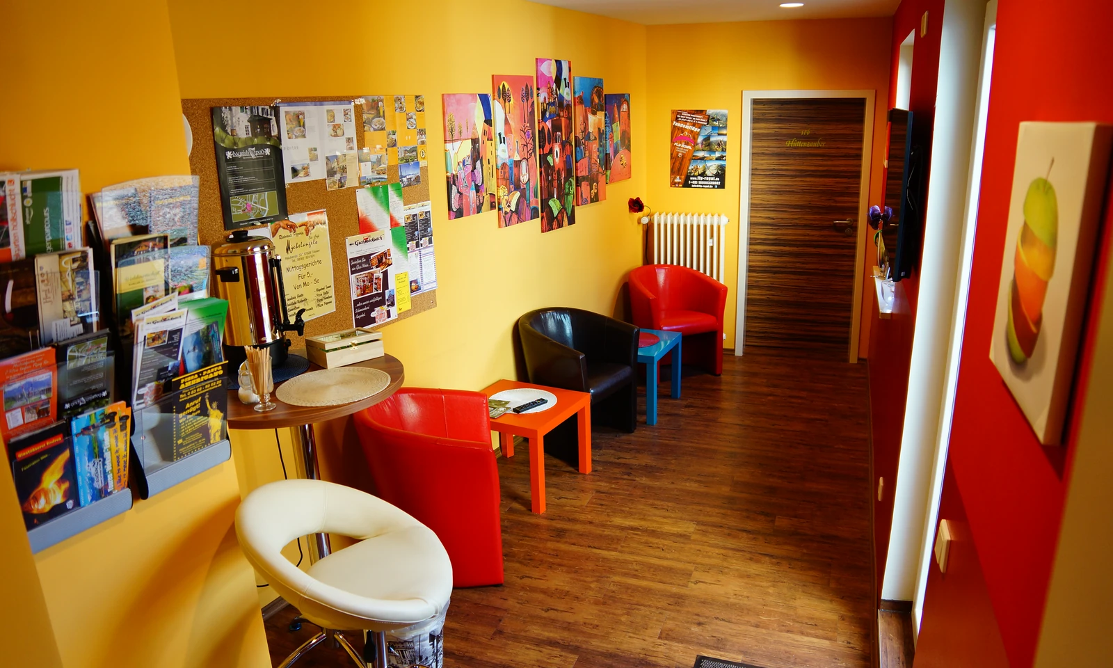 Kleine Lounge mit bunten Sesseln, Beistelltischen und Ausflugstipps an der Wand