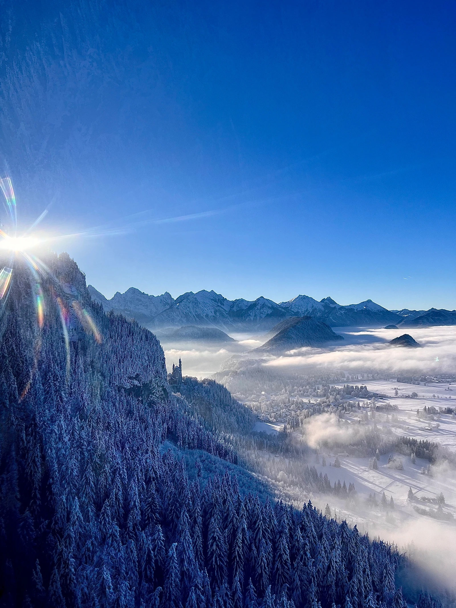 Winterlandschaft mit Schloss Neuschwanstein, verschneiten Bergen und Nebel im Tal