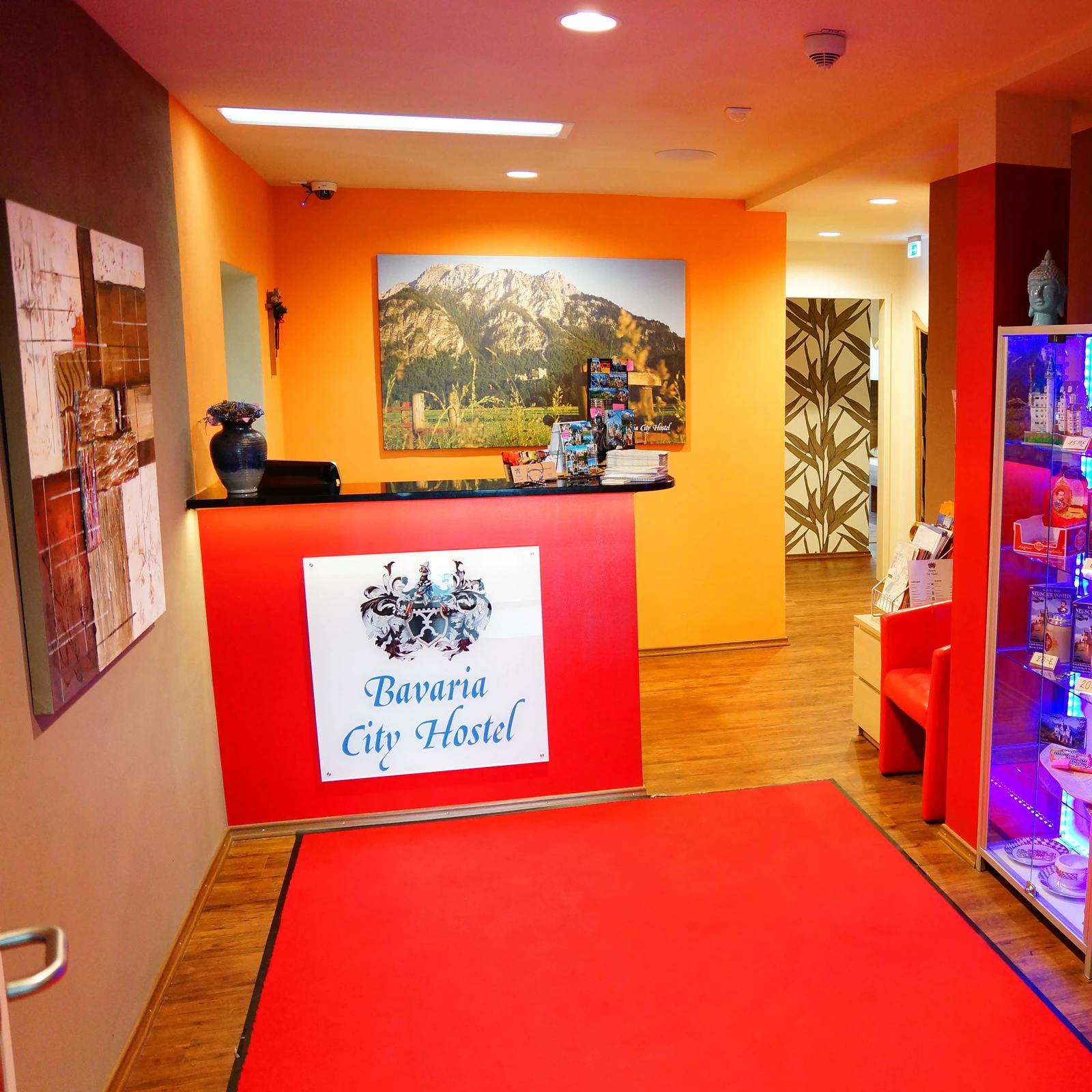Die farbenfrohe Rezeption des Bavaria City Hostel mit rotem Tresen und Familienwappen